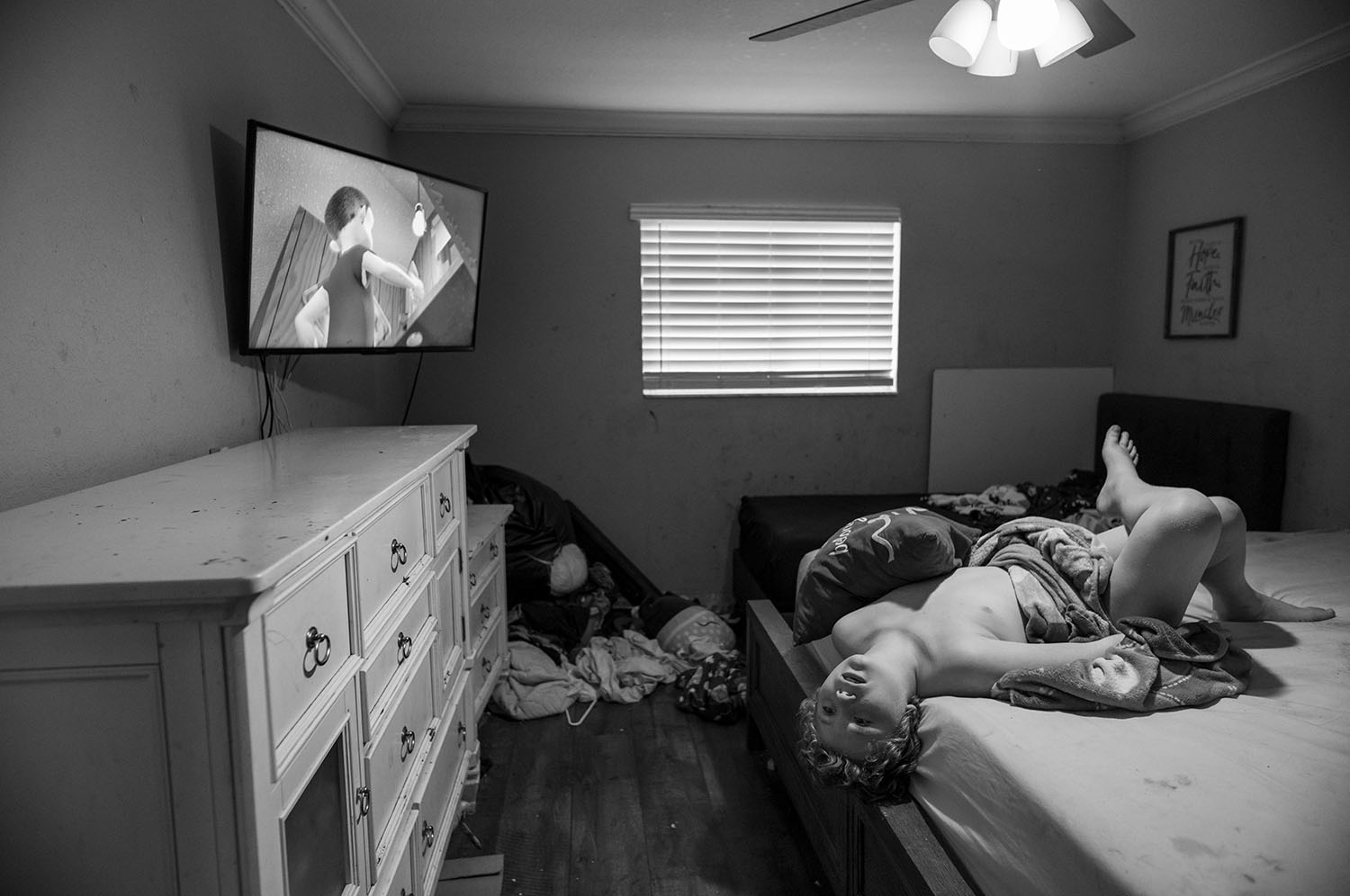 Boy lies on bed with head hanging off the edge.