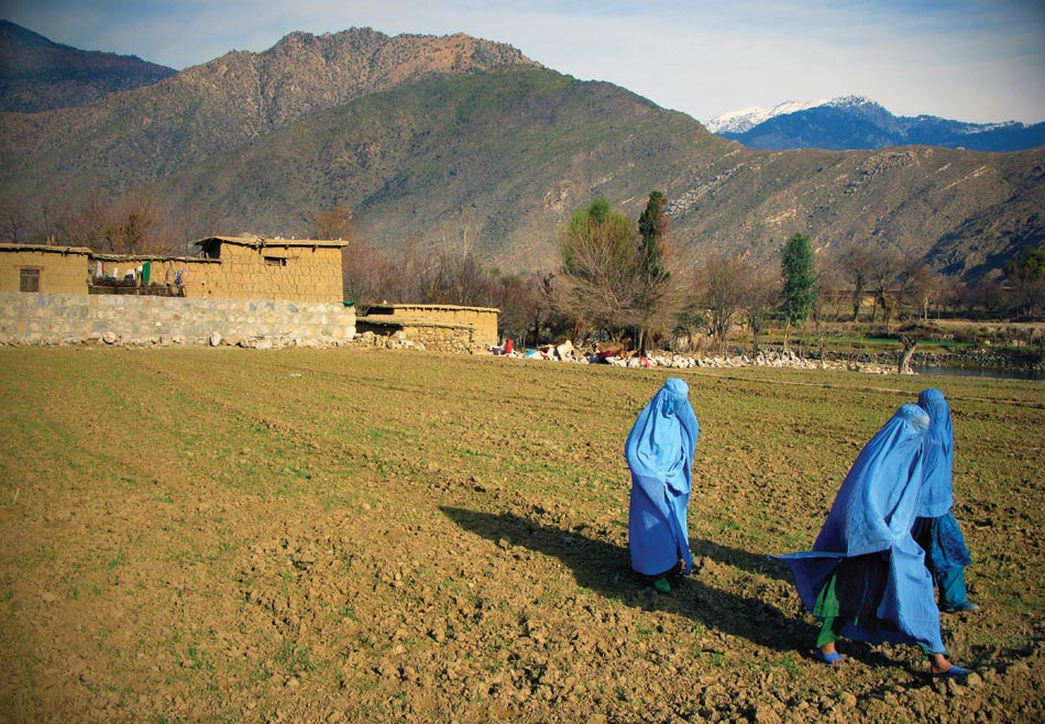 Moving awkwardly across winter fields, avoiding men, women walk to the funeral of a local elder in the Pech Valley near Combat Outpost Honaker-Miracle.