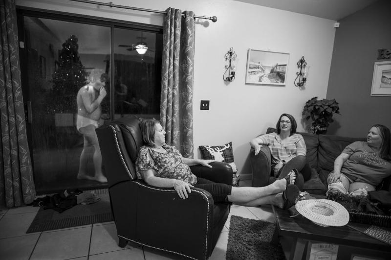 Three women sit in chairs inside. Boy is visible outside through glass door.