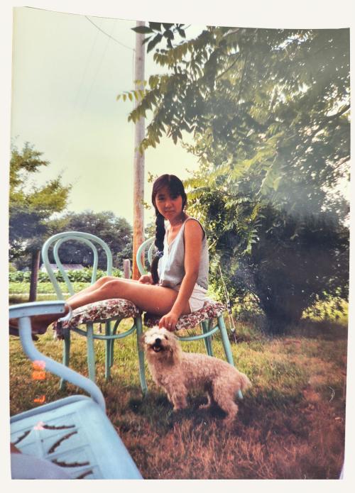 Woman sits on chair with dog beside her.