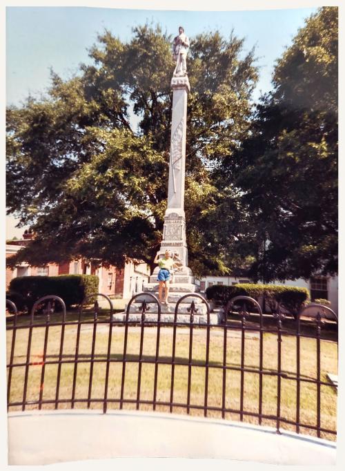 Person stands by monument behind fence.