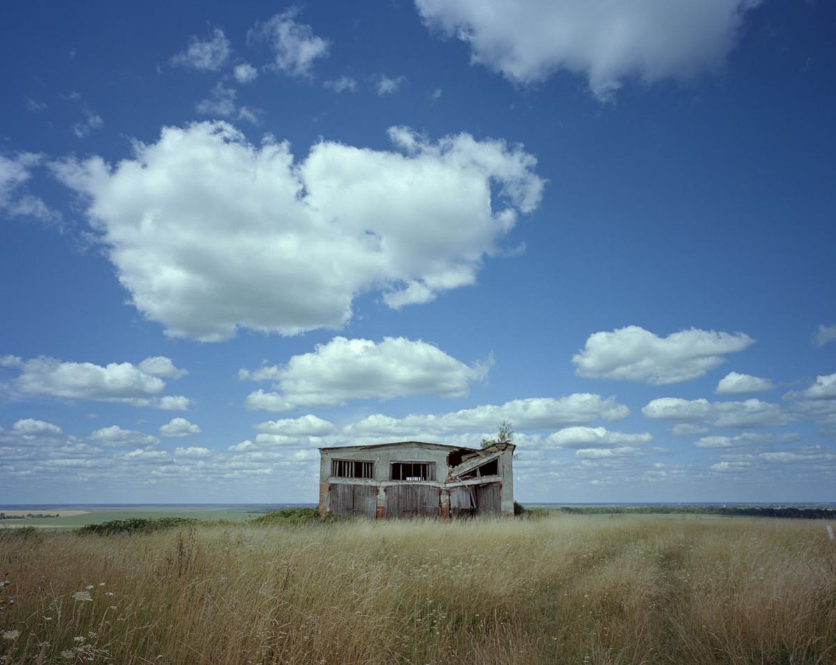 Abandoned building on brown grassy field with blue sky 