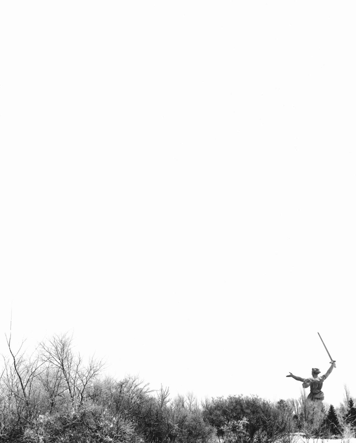 Back of The Motherland Statue in snowy field from afar with bare shrubs in the foreground
