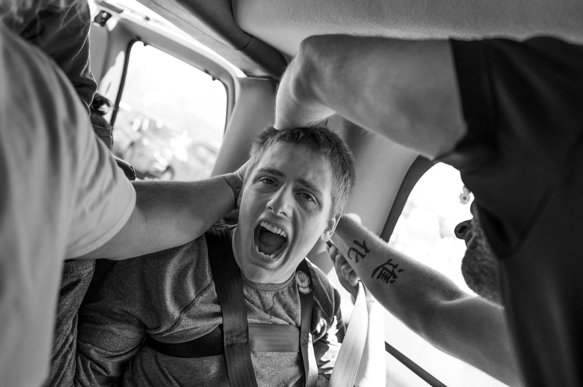 Boy with mouth wide open; two adults keep him in place.